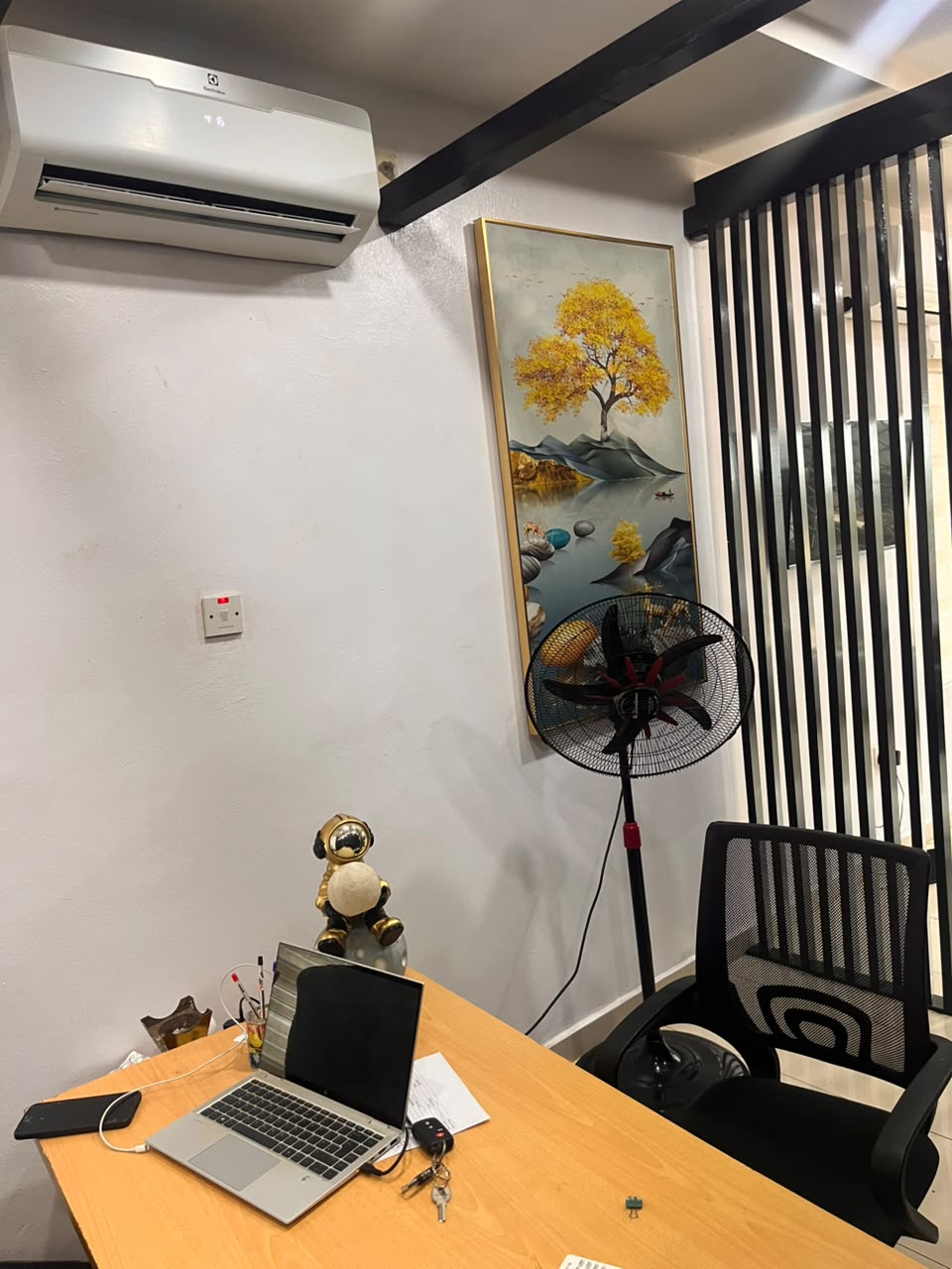 An office desk with a laptop, wall-mounted air conditioner and framed artwork